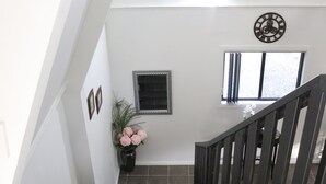 Een trap met zwarte treden en een houten leuning, leidend naar een plateau met een raam en een decoratief muurornament.