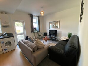 Ett kompakt bostadsutrymme med en soffa, en tv, en tvättmaskin och en matplats.