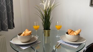 Ett glasbord med två skålar fulla av croissanter, två glas apelsinjuice och en vas med gröna växter.
