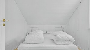 Une petite pièce blanche, avec un lit simple, une porte fermée à clé et une fenêtre avec un cadre en métal.