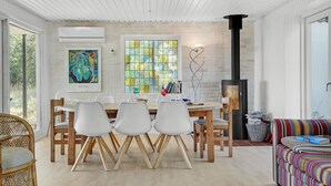 Un espace repas moderne avec une table blanche, quatre chaises blanches et une chaise en bois. On aperçoit une cheminée à l’arrière-plan.