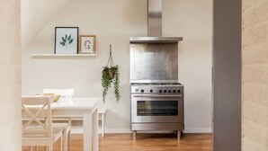 Una cocina con estufa de acero inoxidable, una mesa de comedor blanca con sillas y una planta colgante.