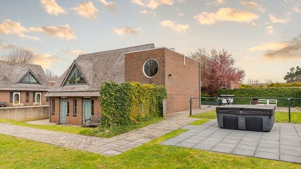 Una casa moderna con fachada de ladrillo, un amplio ventanal circular y un jardín cuidado con zona de patio.