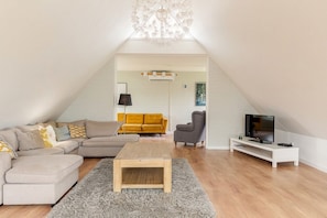A modern living room with a sofa, armchair, and TV, featuring a wooden coffee table and a chandelier.