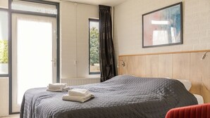 Una habitación de hotel con cama, ventana, puerta y un cuadro en la pared.