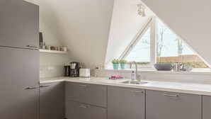 Een moderne keuken met grijze kastjes, een wit aanrecht, een koffiezetapparaat, een broodrooster en een raam met planten.