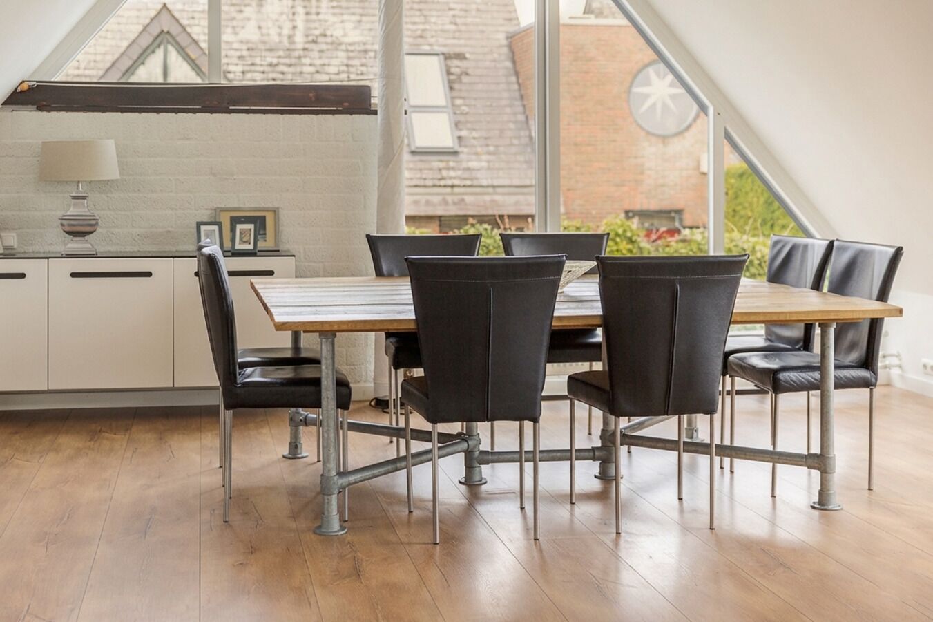 A modern kitchen with a dining table and chairs, a window with a view of a brick building, and a lamp on the counter.