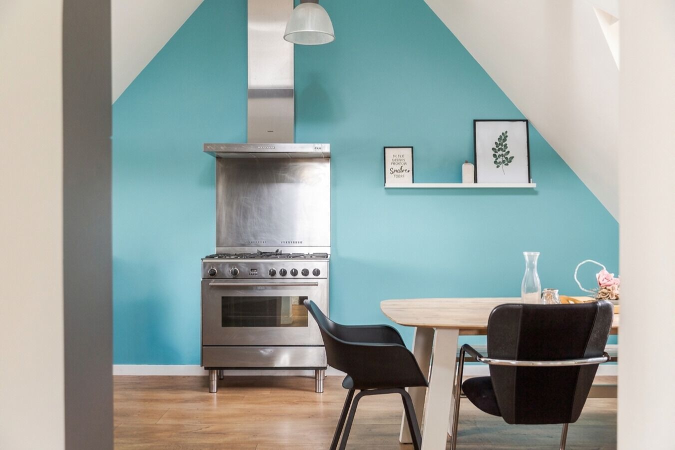 A kitchen with a stainless steel stove, a wooden dining table with two chairs, and a teal accent wall.