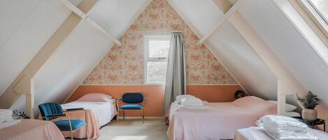 Acogedor dormitorio en ático con dos camas, una silla y un ventanal.
