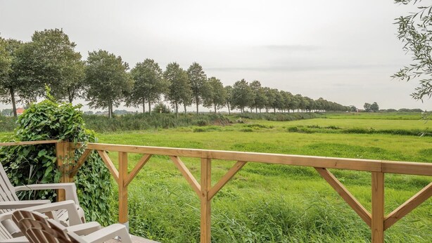 Una terraza de madera con sillas que da a un campo cubierto de césped y  árboles en la distancia.