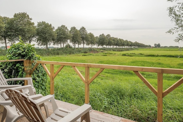 Una terraza de madera con sillas que da a un campo cubierto de césped y árboles en la distancia.