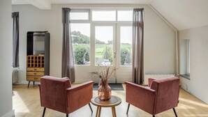 Una habitación amplia con un gran ventanal, dos sillones, una mesita redonda y un aparador.