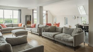 Amplia sala de estar con un sofá modular grande, comedor con mesa y sillas, y vista al exterior a través de amplias ventanas.