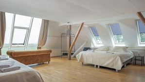 Un espacioso dormitorio en el ático con una cama grande, un sofá antiguo y vistas al exterior.
