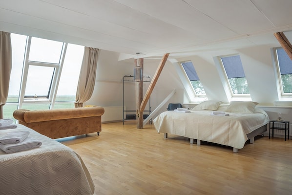 Une chambre spacieuse située sous les combles, avec un grand lit, un canapé d’époque et une vue sur l’extérieur.
