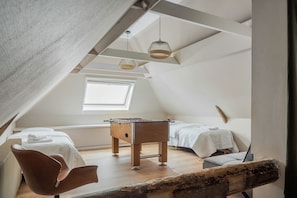Une chambre confortable située dans les combles, avec un baby-foot, deux lits, une chaise et une grande fenêtre.