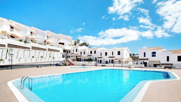A swimming pool surrounded by white buildings with balconies, under a clear sky. - Remarkable 2-bed House in Chayofa With Pool (Arona)