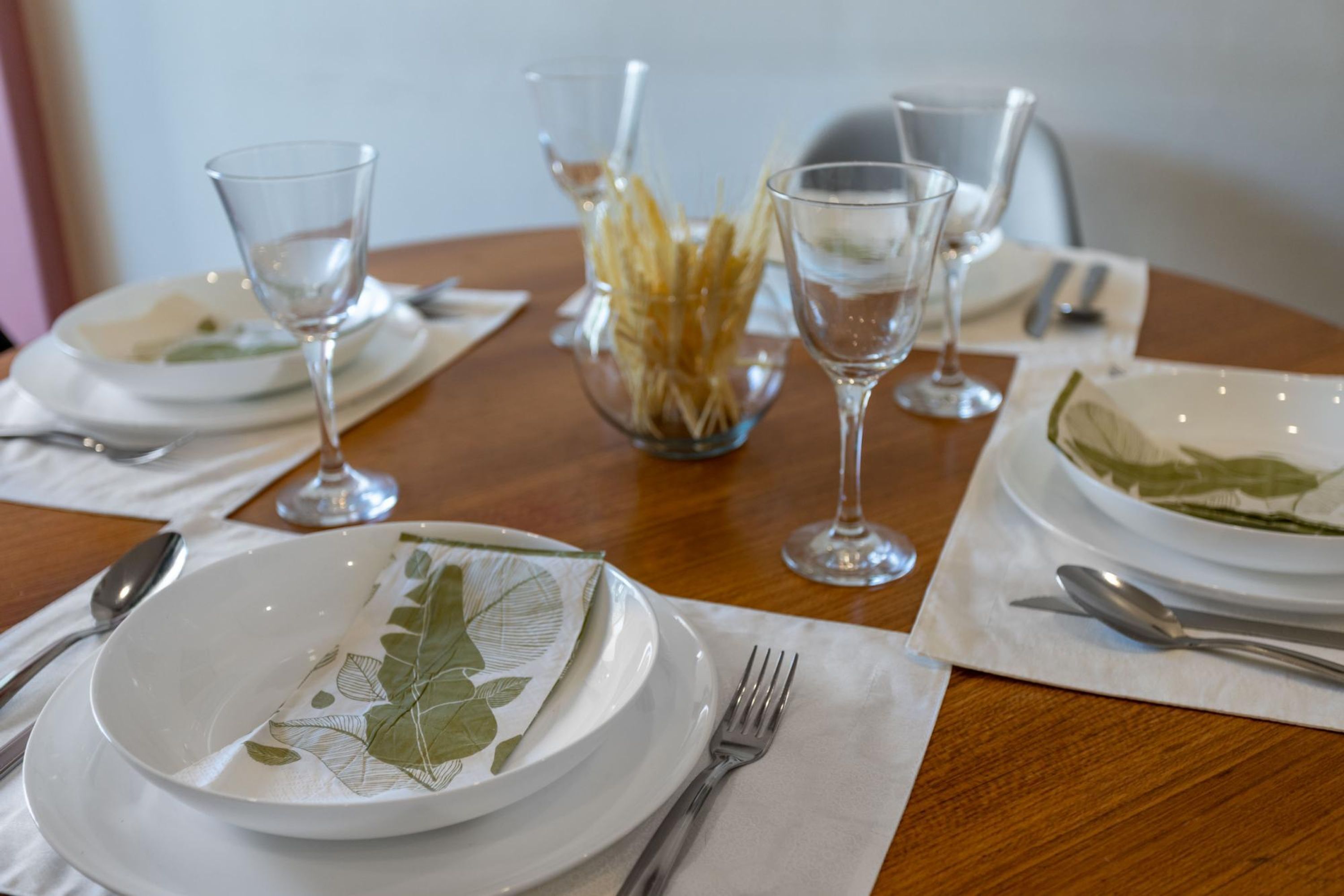 Una mesa de comedor dispuesta con platos, cubiertos y copas de vino.