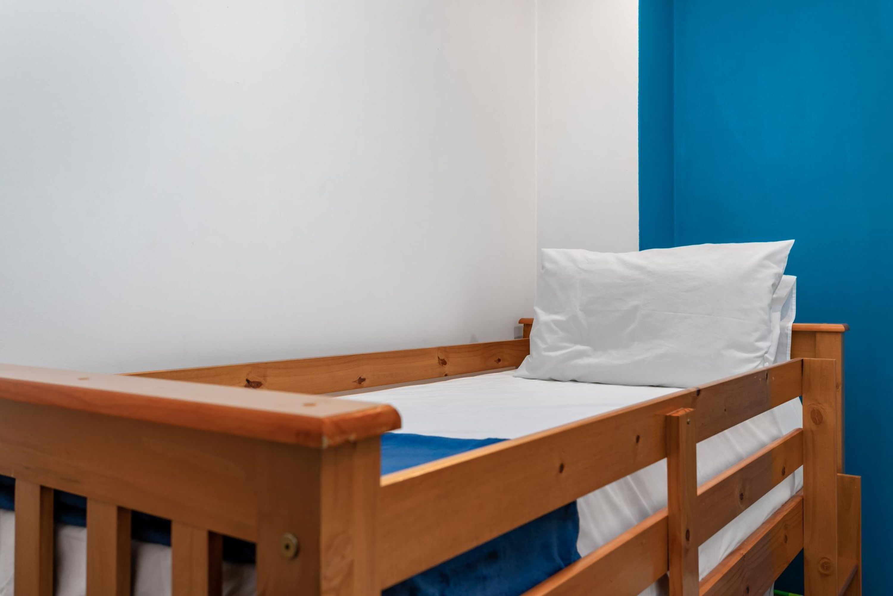 Una cama de madera individual con ropa de cama blanca en una habitación con paredes azules.