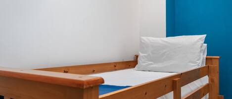 Una cama de madera individual con ropa de cama blanca en una habitación con paredes azules.
