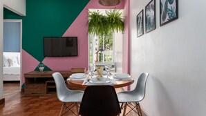 A dining area with a wooden table set for four, surrounded by white chairs. A large window provides natural light, and a hanging plant adds greenery. - 6 Minutes From Copacabana Beach Rdl1112 (Rio de Janeiro)