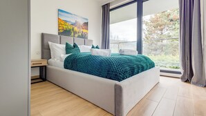 Een moderne slaapkamer met een groot bed, een nachtkastje, een schilderij en uitzicht op de omgeving.