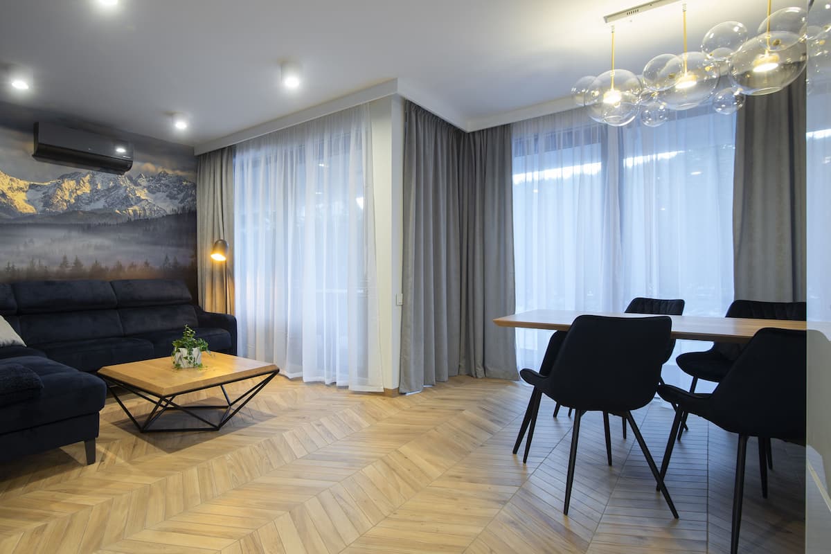 Een moderne woonkamer met een donkerblauwe bank, een houten salontafel en een eethoek met een tafel en stoelen.