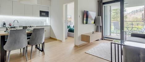 Una cocina moderna con microondas, comedor con sillas, un sofá y un balcón con vista a árboles.