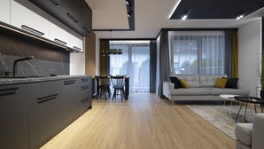 Een moderne keuken met donkere kasten en een marmeren aanrecht, een eethoek met een houten tafel en stoelen, en een zithoek met een bank en salontafel.