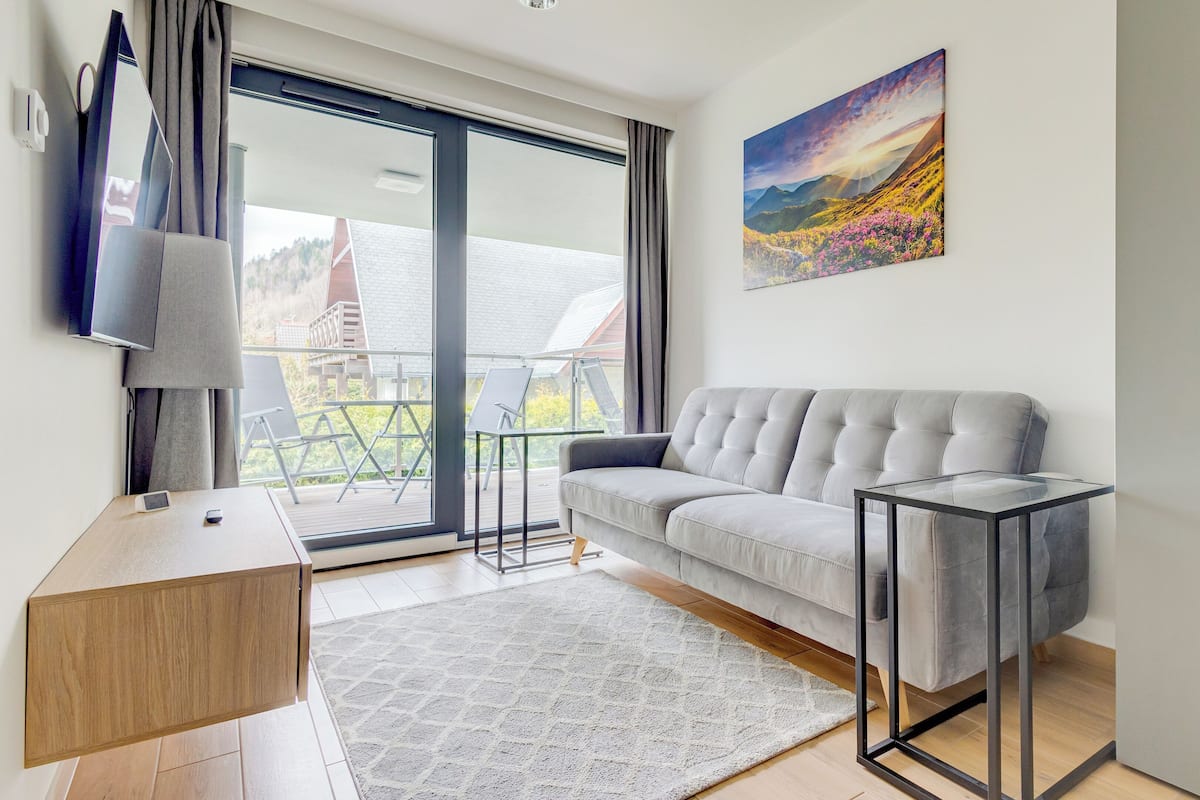 Een moderne woonkamer met een grijze bank, een glazen salontafel en een schilderij aan de muur.
