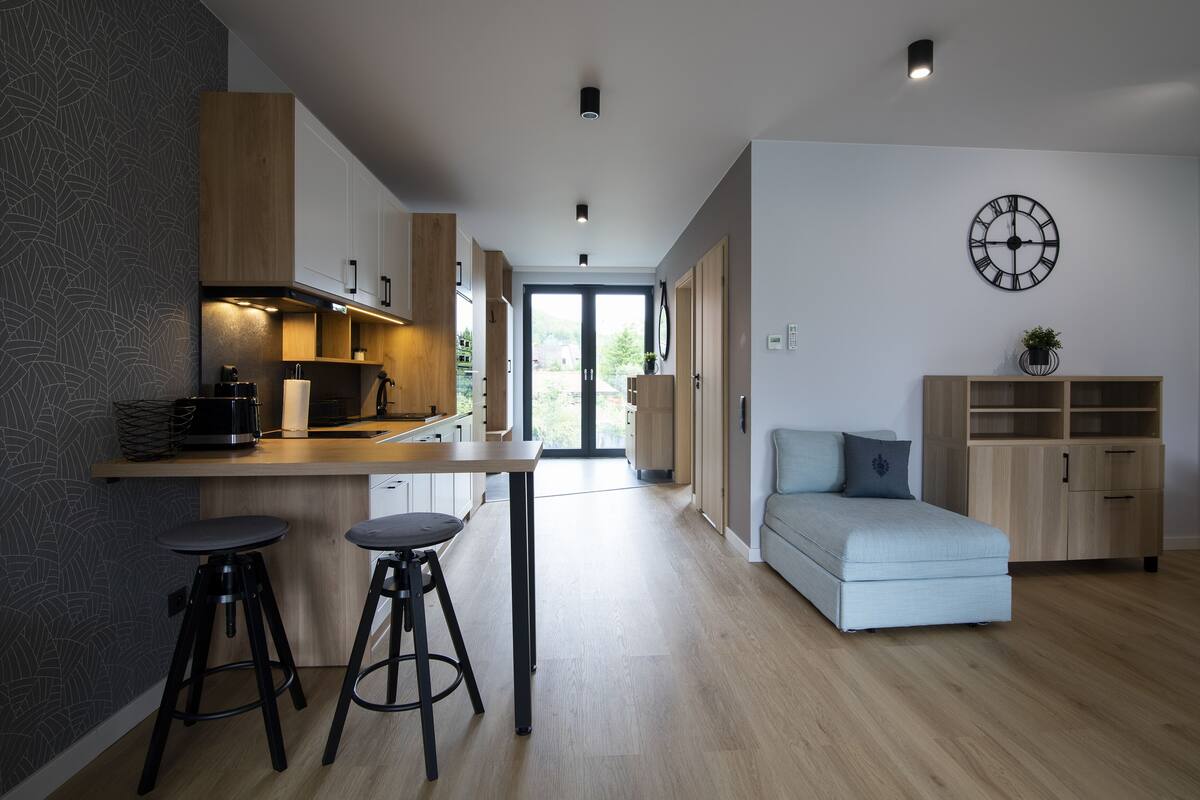Een moderne keuken met een centraal eiland, twee barkrukken en een lichtblauwe bank in een ruime woonkamer.