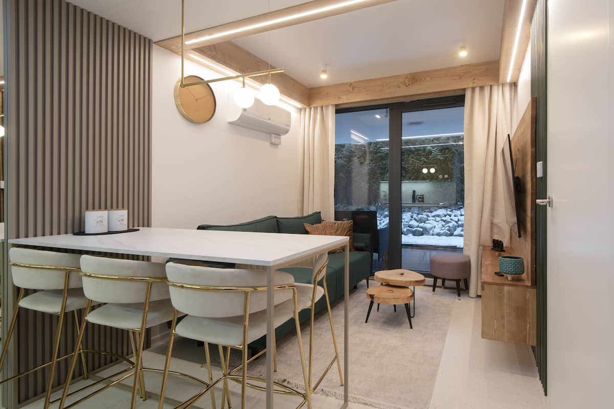 Een moderne keuken met een wit aanrecht, goudkleurige stoelen en een houten eettafel.