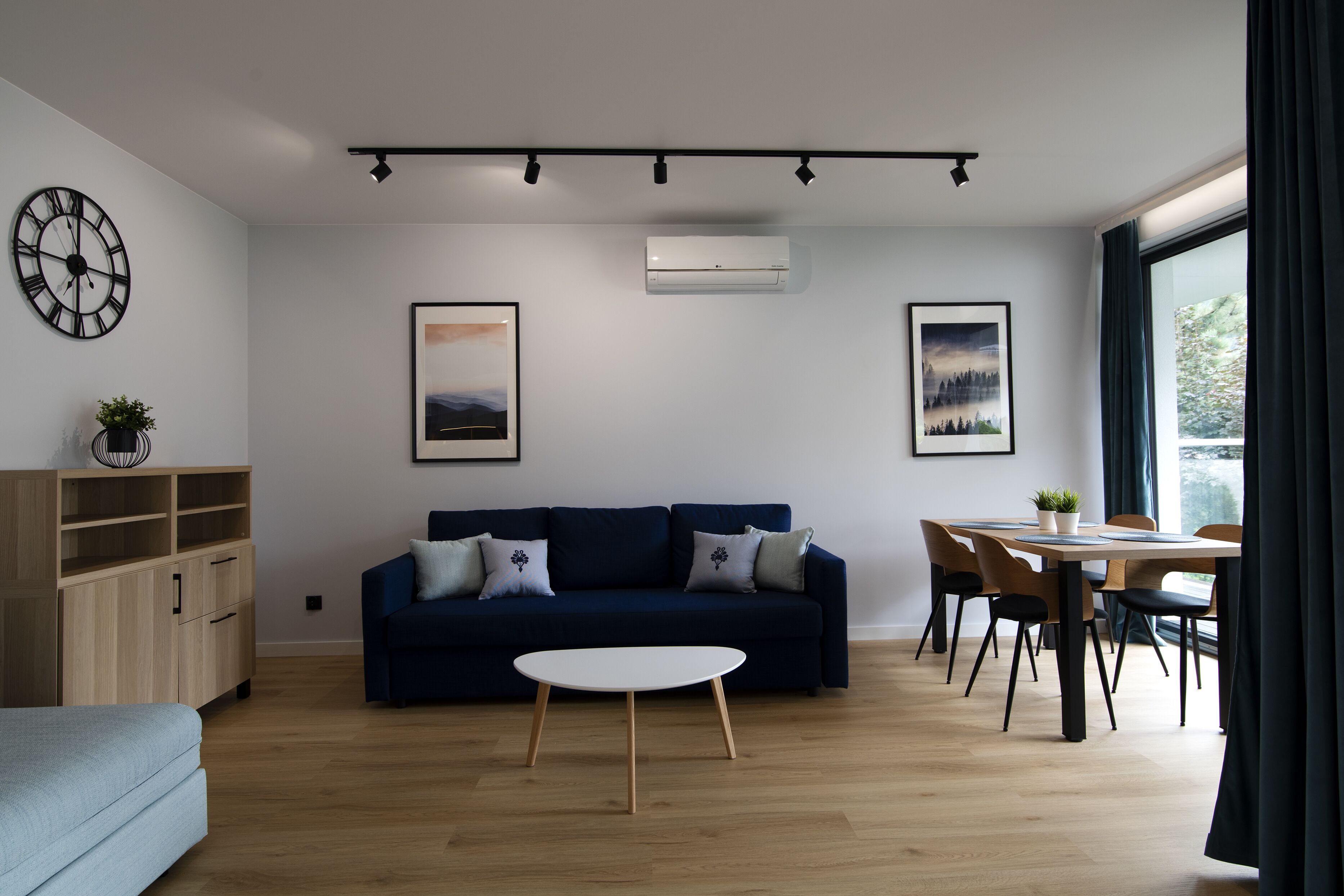 A modern living room with a dark blue sofa, a round white coffee table, and a dining area with a wooden table and chairs.