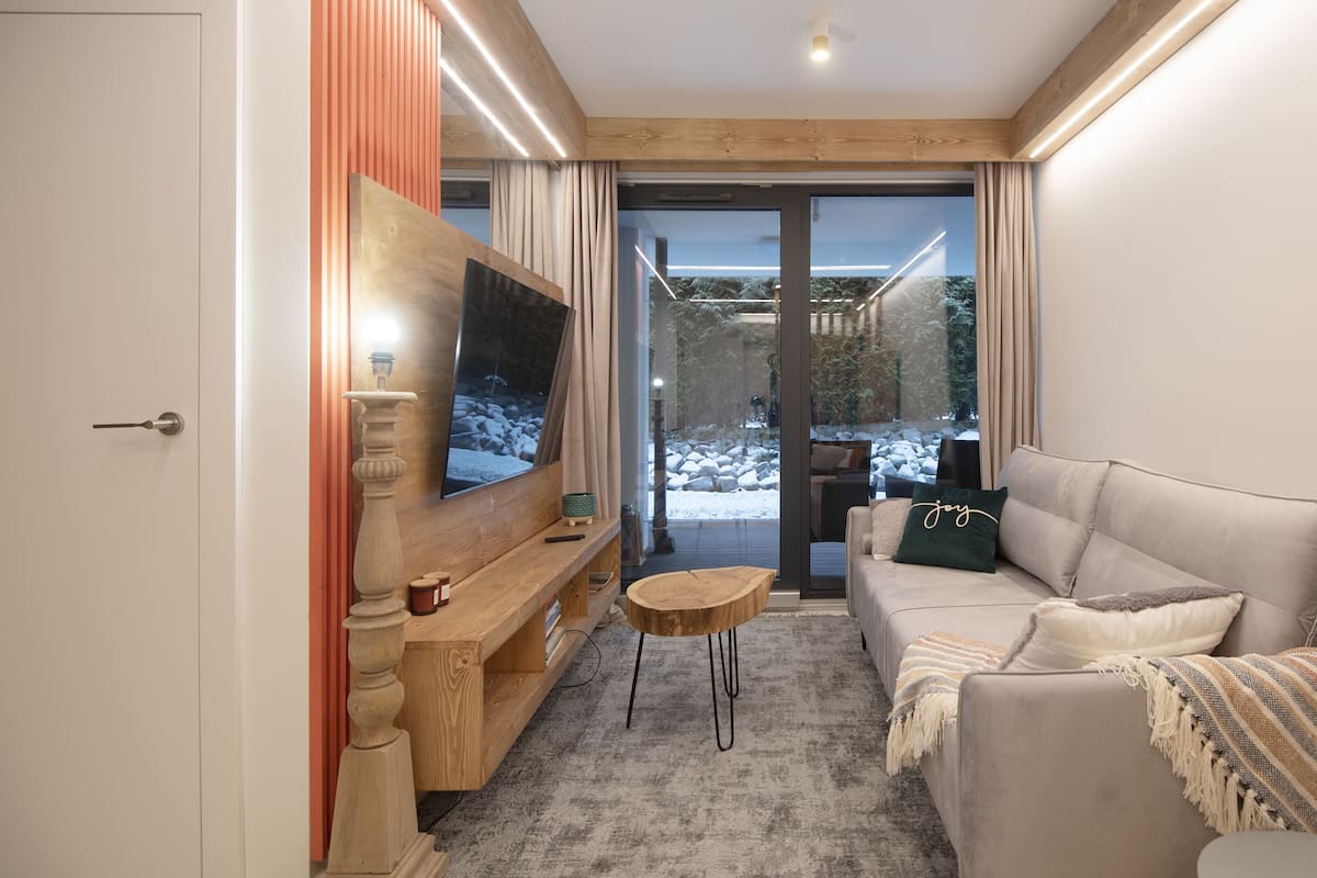 Een moderne woonkamer met een grote flatscreen televisie, een houten salontafel en een beige bank met een plaid.
