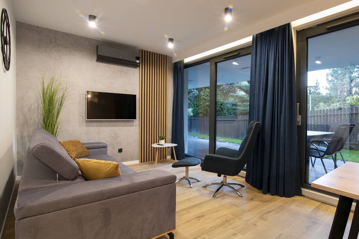 Een moderne woonkamer met een grijze bank, een flatscreen televisie, een bijzettafeltje en een stoel.