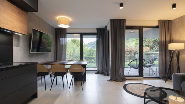Een moderne leefruimte met een eethoek, een flatscreen televisie en een balkon met uitzicht op groen.