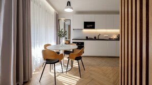 Een moderne keuken met witte kasten, een zwart aanrecht en een ingebouwde oven. Er is een eethoek met een ronde tafel en vier stoelen.