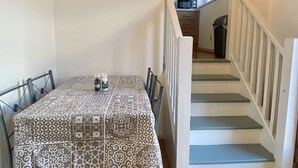 Una zona de menjador amb un mantell estampat, un conjunt de cadires i una escala que condueix a una cuina.