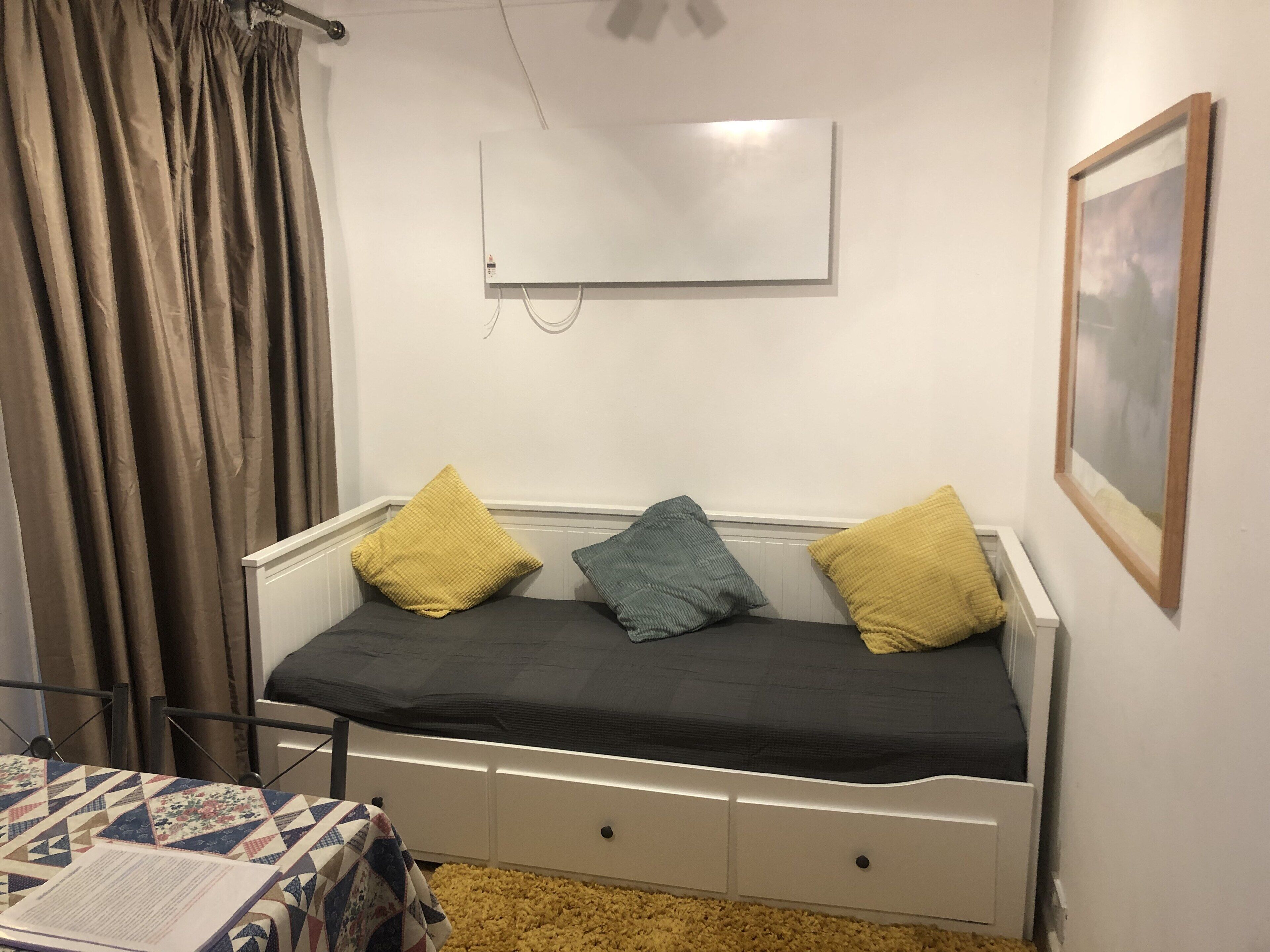 Una habitación pequeña y sencilla con una cama, una mesa con colcha y un radiador.