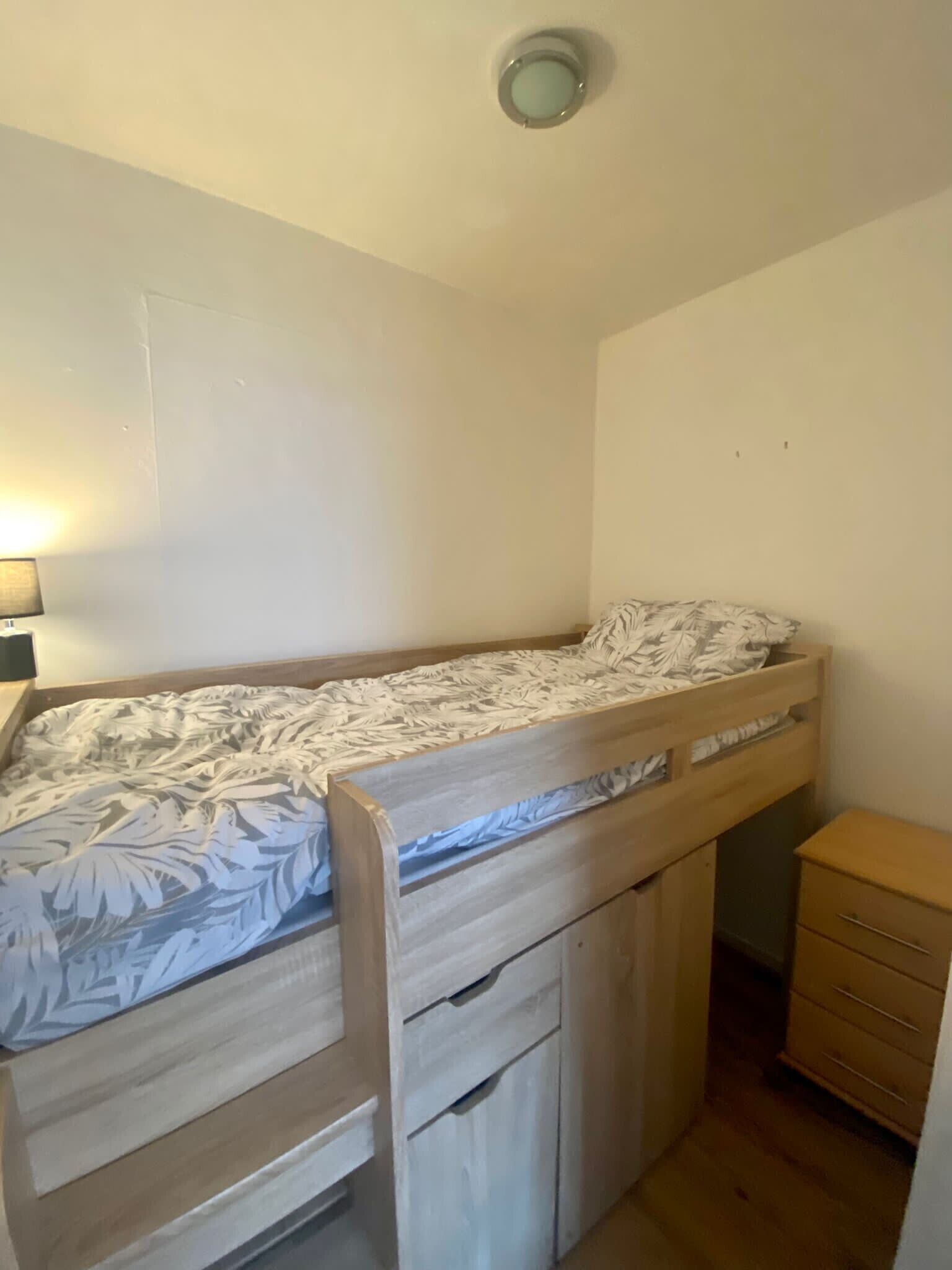 Un lit superposé avec un tiroir de rangement en dessous, une table de chevet et une petite armoire en bois.
