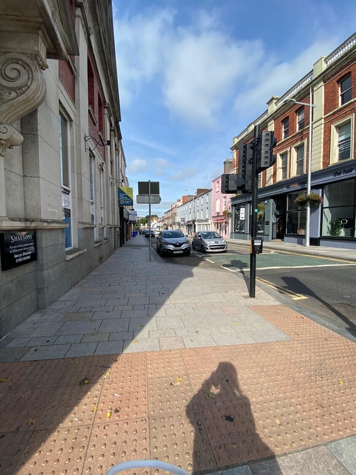 A street view with a sidewalk, parked cars, and buildings with storefronts.