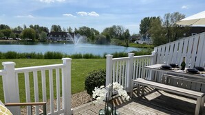 A deck with a table set for dining, overlooking a lake with a fountain.