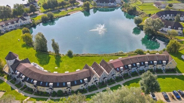 A large, curved building with a central courtyard and a lake.