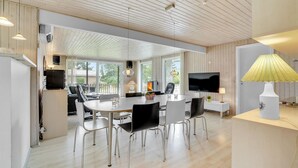Une cuisine moderne dotée d’un îlot central, d’un coin repas avec une table ronde et des chaises, et d’un téléviseur fixé au mur.