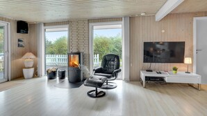 Un salon moderne avec un poêle à bois, un fauteuil en cuir confortable, un téléviseur à écran plat et une console blanche.