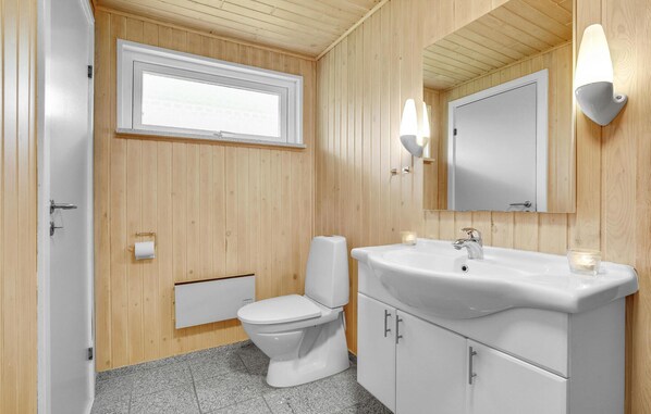 A bathroom with wooden paneling, a toilet, a sink with a mirror, and a window.