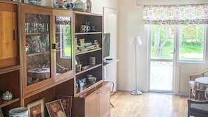 A room with a wooden cabinet with glass doors, a television, and a window with a floral curtain. - Cozy home in gärsnäs with WiFi (GÄRSNÄS)