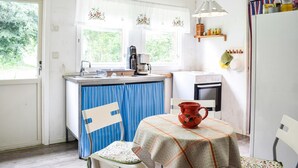 A compact kitchen with a sink, a coffee maker, and a small oven. There is a table with a red mug and a chair with a floral cushion. - Cozy home in gärsnäs with WiFi (GÄRSNÄS)