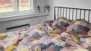 A bed with a colorful quilt, a window with a view of trees, and a bedside table with a lamp. - Cozy home in gärsnäs with WiFi (GÄRSNÄS)