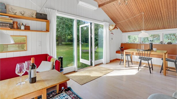 A spacious living area with a wooden ceiling, a dining table with chairs, a red sofa, and a large sliding glass door leading to a garden. - 1 bedroom awesome home in Jægerspris (Jægerspris)